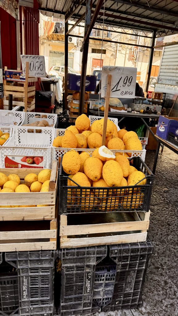 Ein Marktstand mit mehreren Kisten, die große, gelbe Früchte enthalten. Preisschilder geben an, dass die gelben Früchte 1,99 Euro kosten und andere Kisten Kartoffeln für 0,65 Euro anbieten.
